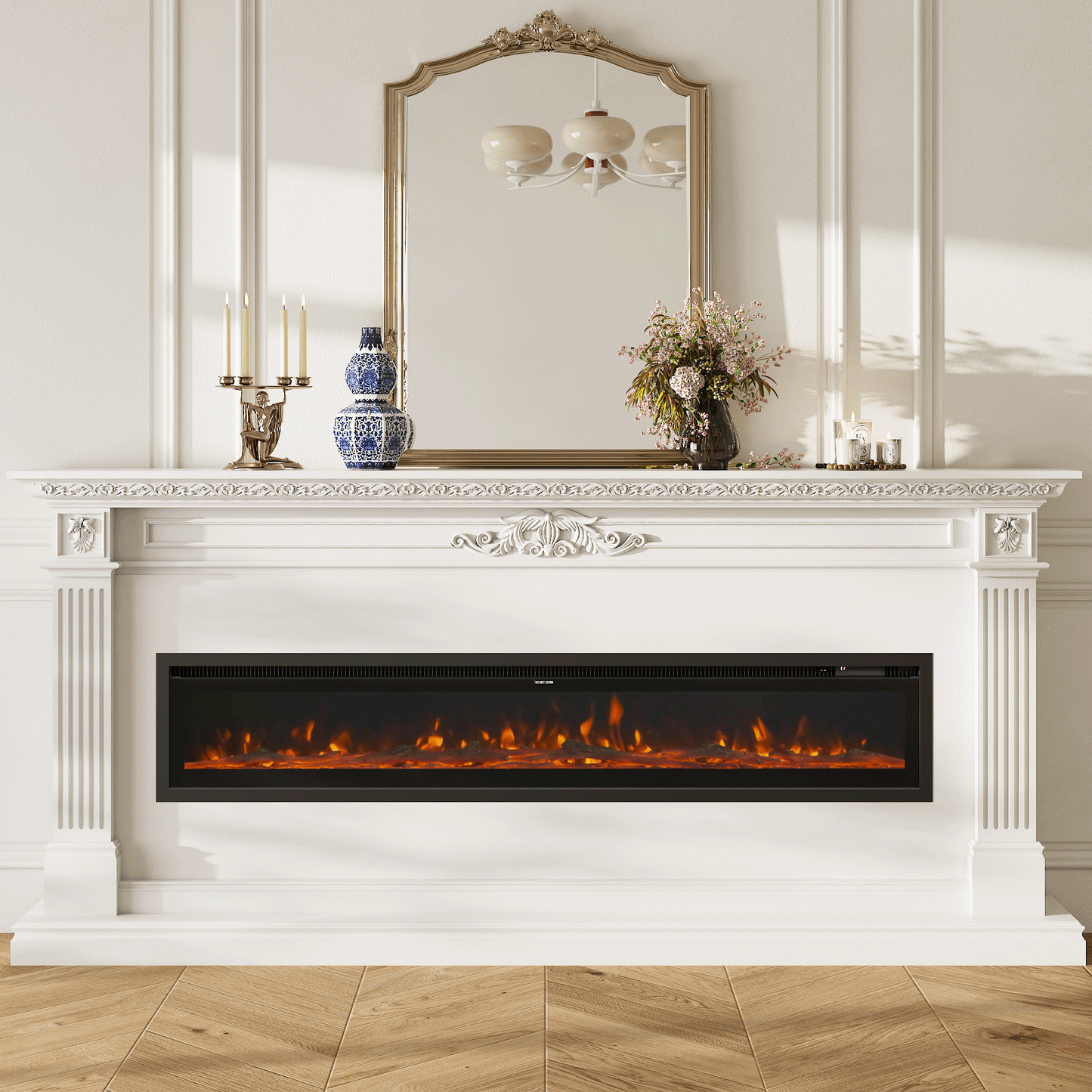 Elegant media wall with a recessed electric fireplace featuring vibrant orange flames, framed by a white ornate mantel, decorated with a vintage mirror, candelabra, and floral accents.