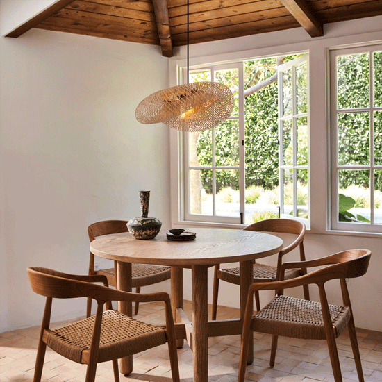 bamboo pendant light above a round wooden dining table by large windows